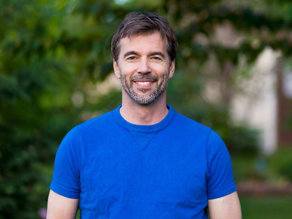 A man wearing a blue shirt smiles warmly at the camera.